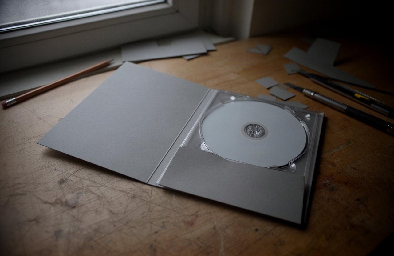 Rozłożony kartonowy digipack z plastikową tacką i płytą na drewnianym stole w domowym studiu